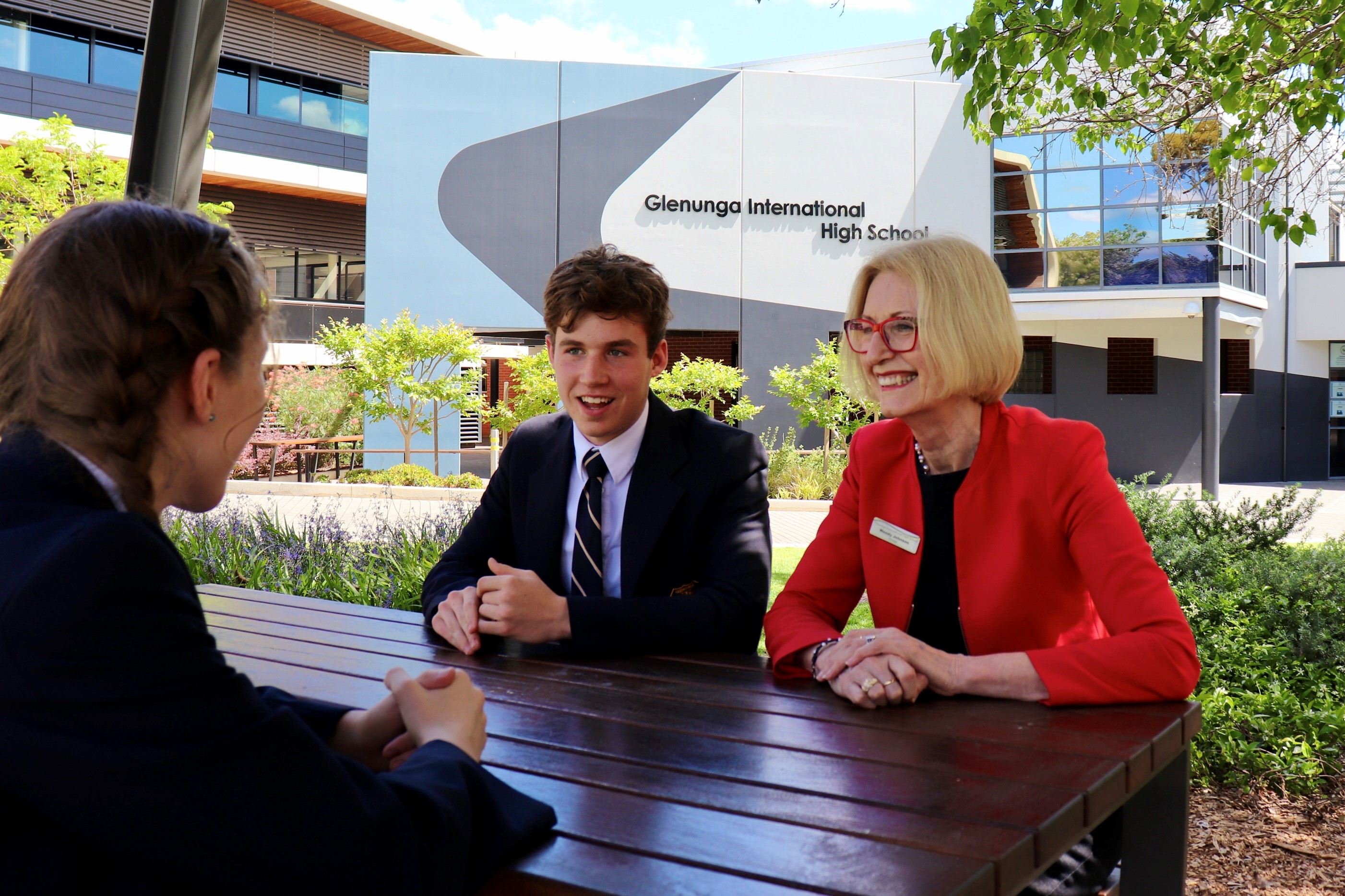 Ms Wendy Johnson sitting outside with two students from Glenunga International High School   