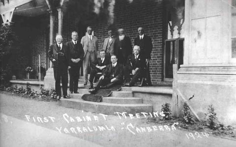 a black and white photo of 6 men standing and 3 seated on steps. All are dressed in 1920's style suits
