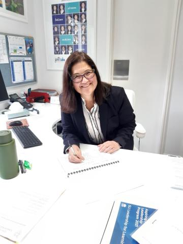 Mechel Pikoulas, seated, smiling at her desk