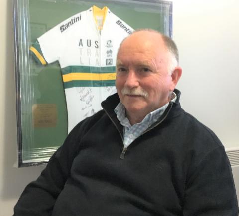 Noel Pearce, smiling, with framed cycling jersey behind him
