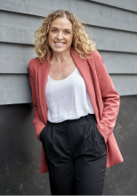 A woman wearing a pink coat and white shirt leaning against a wall